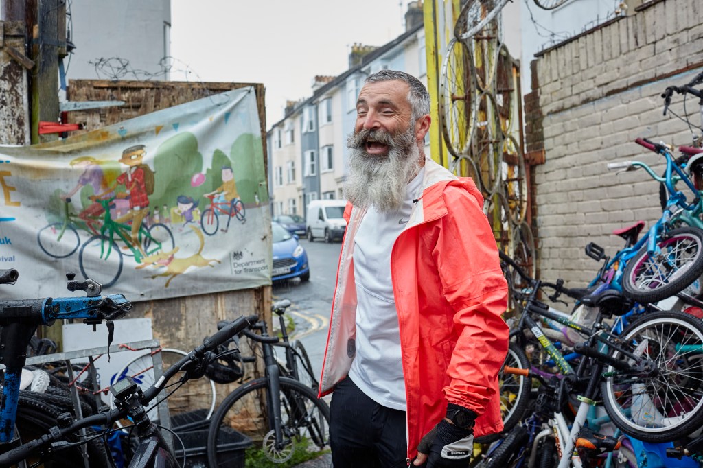 A volunteer in Brighton Bike Hub is laughing surrounded by bicycles
